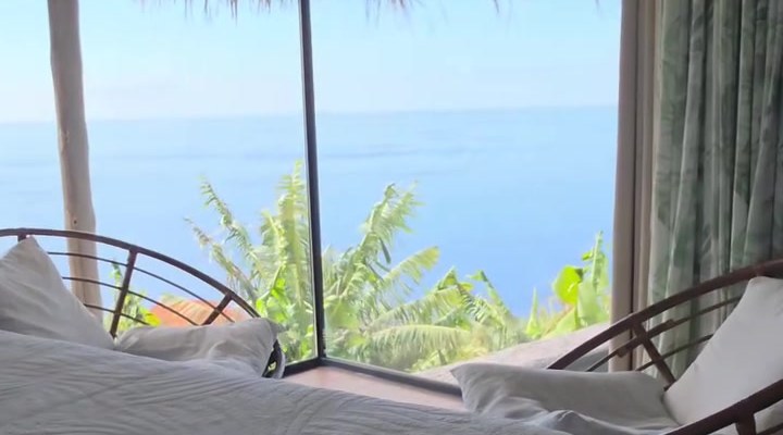 Bed facing large windows with the sea beyond