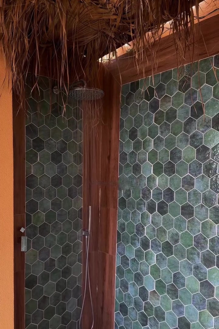The outdoor rain shower with green hexagonal tiles under the thatched roof